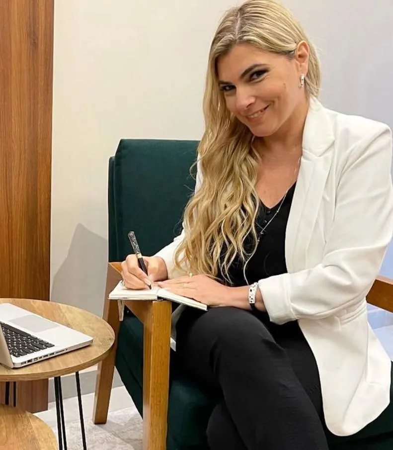 Daniela Bizari, sentada em uma poltrona, escrevendo em um bloco