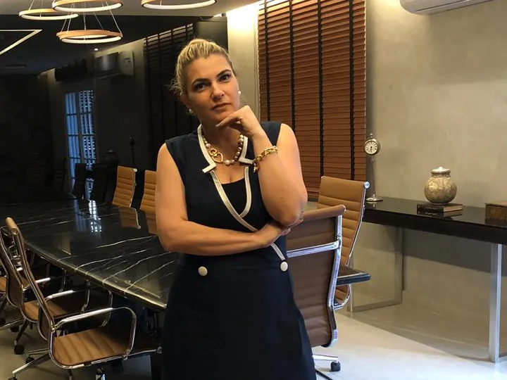 Daniela Bizari em pé na sala de reunião, ao lado da mesa preta