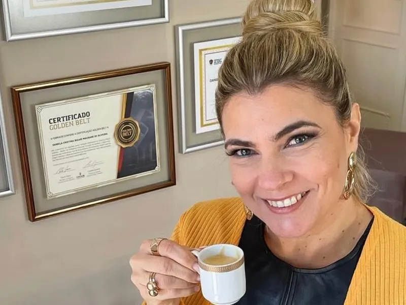 Daniela Bizari no escritório, com uma xícara de café e certificados ao fundo